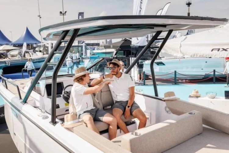 Slide: The Image of 2027 Axopar 25 Cross Top boat with two people relaxing onboard at a marina. - 7