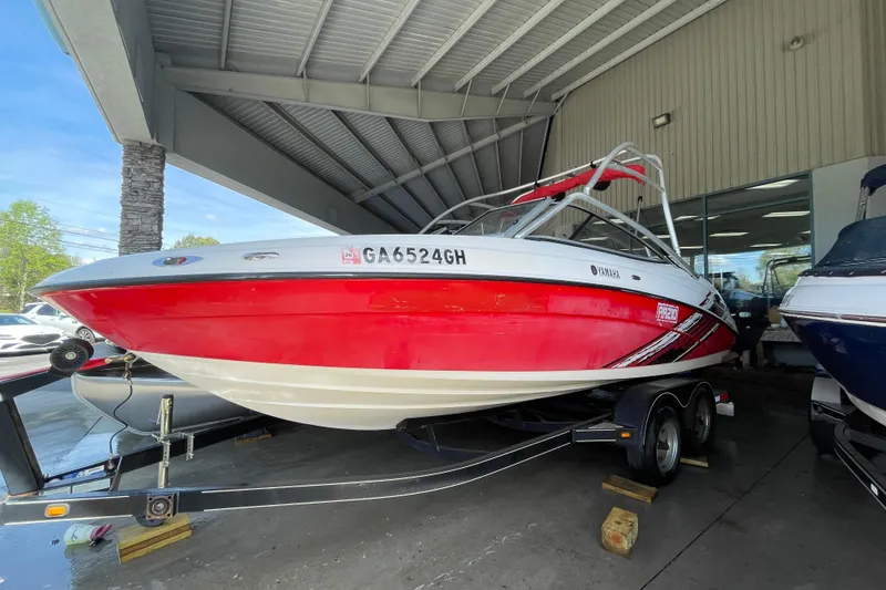 The Image of 2008 Yamaha AR210 boat in red and white, displayed on a trailer under a shelter. - 0