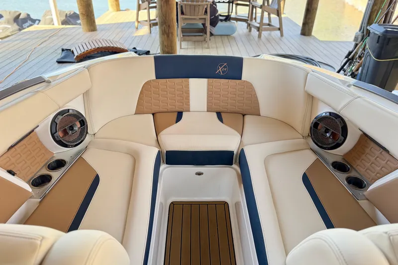 Slide: The Image of 2022 MasterCraft X24 boat interior with beige and navy seating, cup holders, and speakers. - 23