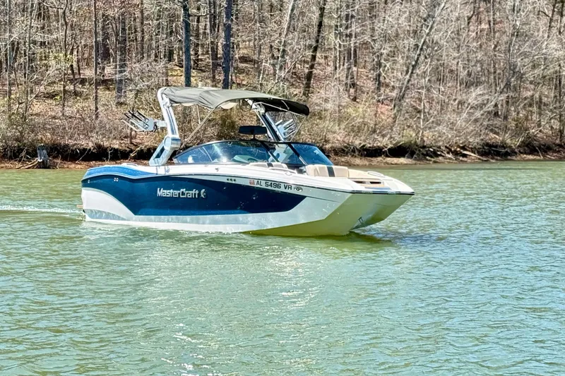 Slide: The Image of 2022 MasterCraft X24 boat cruising on a serene lake with wooded shoreline. - 4