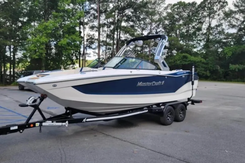 Slide: The Image of 2022 MasterCraft X24 boat on trailer in parking lot, surrounded by trees. - 41