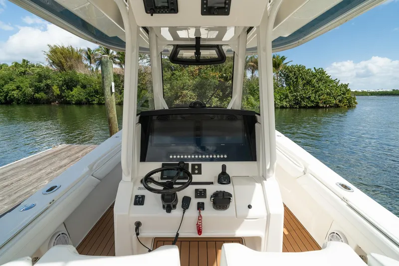 Slide: The Image of 2020 Regulator 31 boat cockpit with steering wheel and controls, docked by lush greenery. - 35