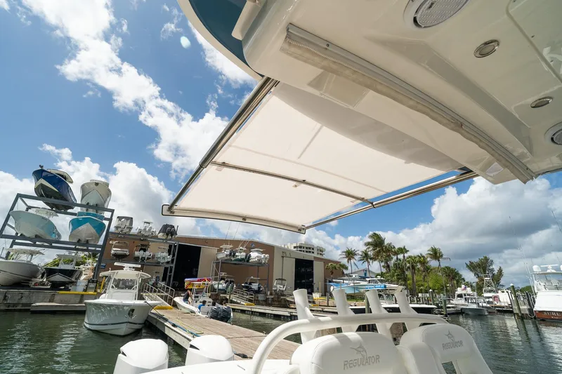 Slide: The Image of 2020 Regulator 31 boat with sunshade at marina, clear sky, and docked vessels. - 70