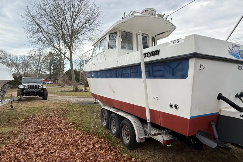 Slide: The Image of 2005 Osprey 28 Long Cabin boat on trailer, parked near a Jeep, surrounded by trees. - 3