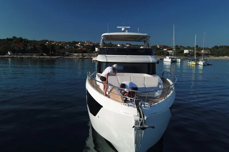 Slide: The Image of 2026 Absolute Navetta 70 yacht docked with two people on deck, scenic coastal backdrop. - 6