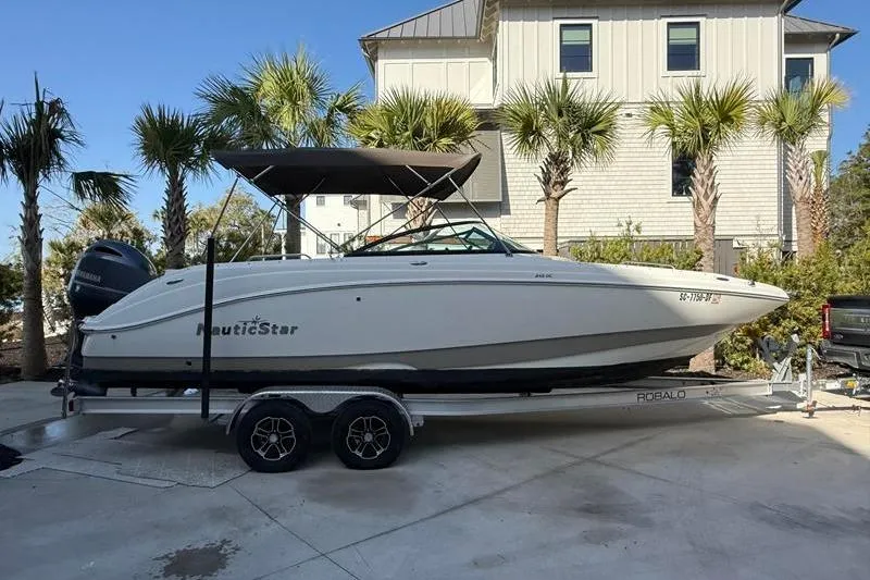 The Image of 2017 NauticStar 243DC Sport Deck boat on trailer, parked near palm trees. - 1