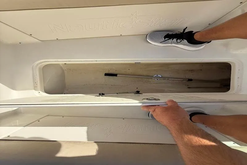 Slide: The Image of 2017 NauticStar 243DC Sport Deck storage compartment with open hatch and visible equipment. - 25