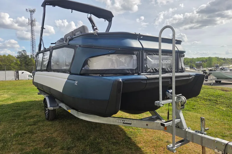 Slide: The Image of 2024 Sea-Doo Switch Cruise 21 on trailer, parked on grassy area under cloudy sky. - 2