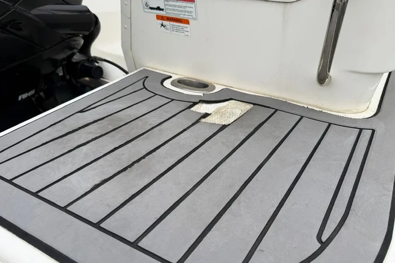 Slide: The Image of 2019 Striper 230 DC boat deck with wear and tear, featuring a damaged mat. - 7