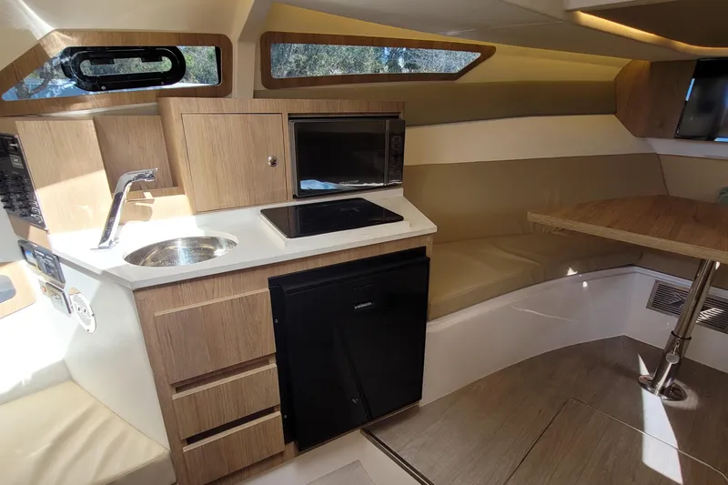 Slide: The Image of 2023 NX Boats NX340 interior with kitchenette, featuring sink, stove, microwave, and seating area. - 16