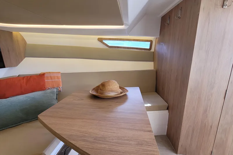 Slide: The Image of Interior of 2023 NX Boats NX340 with wooden table, cushions, and a straw hat. - 18