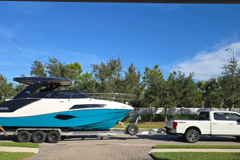 Slide: The Image of 2023 NX Boats NX340 on trailer, towed by a white pickup truck under clear blue sky. - 4