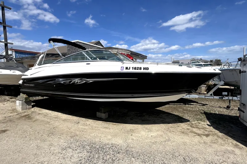 The Image of 2011 Monterey 254FSC boat on blocks, black and white exterior, parked outdoors. - 0