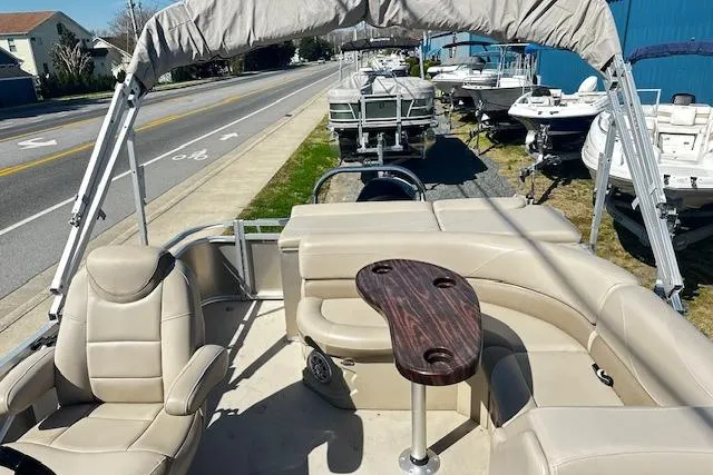 Slide: The Image of 2016 Avalon LSV Tri Toon boat with beige seating and a wooden table, parked near a road. - 4