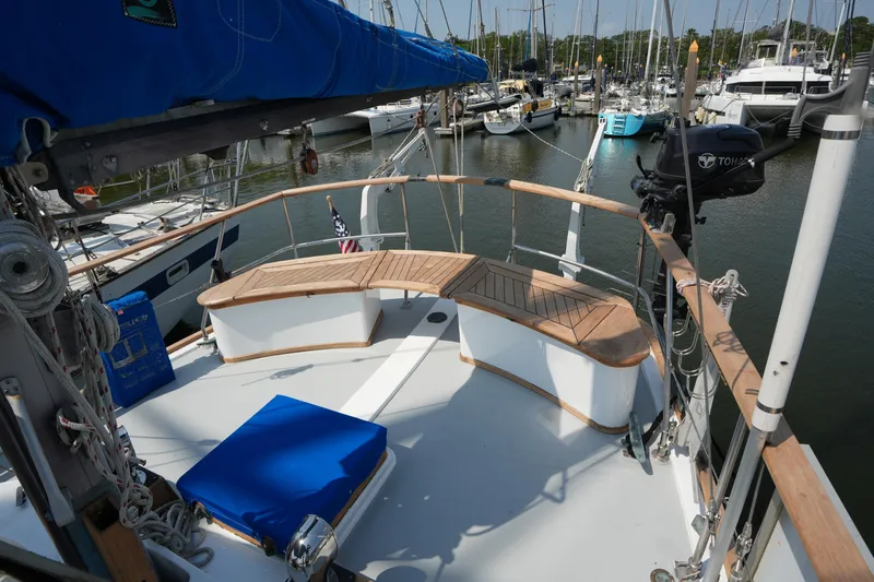 Slide: The Image of 1982 Vagabond 47 sailboat deck with wooden seating and blue cushion in marina. - 15
