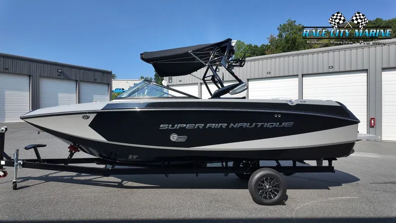 Slide: The Image of A black 2013 Nautique G23 boat on a trailer in front of garages. - 2