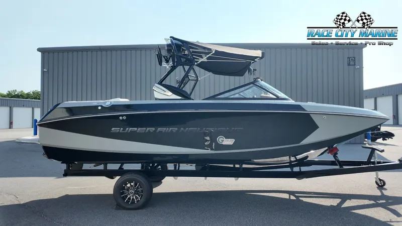 The Image of A black 2013 Nautique G23 boat on a trailer in front of a gray building. - 1