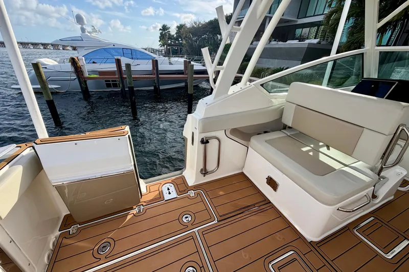 Slide: The Image of 2022 Boston Whaler 280 Vantage boat interior with seating and teak flooring, docked by the water. - 9