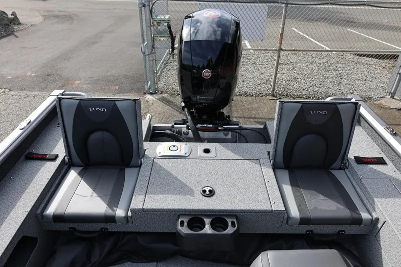 Slide: The Image of 2026 Lund 1875 Impact XS Sport boat interior with seating and motor, parked near a fence. - 22