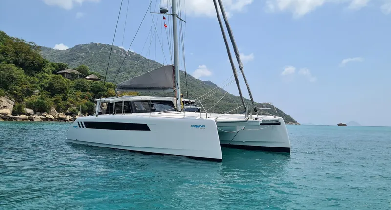 Slide: The Image of 2025 Seawind 1370 catamaran sailing in clear blue waters near a lush, mountainous coastline. - 1