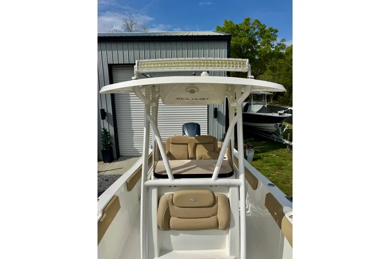 Slide: The Image of 2016 Sea Hunt Ultra 234 boat with T-top and seating, parked near a metal building. - 5