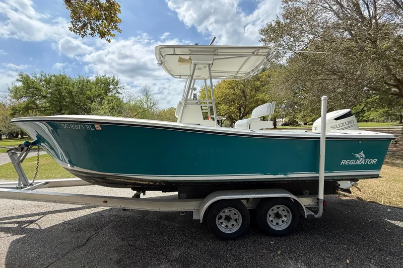 Slide: The Image of 1997 Regulator 23 boat on trailer, teal hull, Suzuki outboard motor, parked outdoors. - 3
