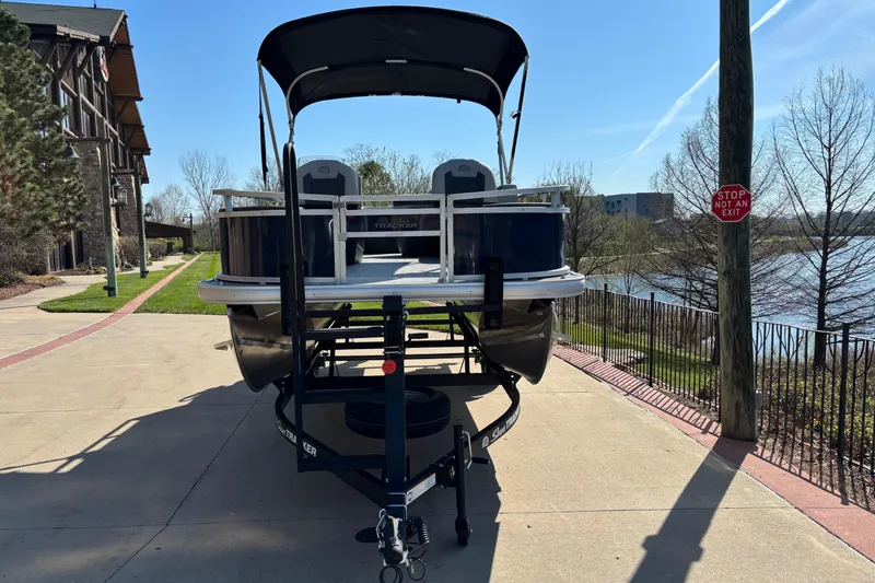 Slide: The Image of 2026 Sun Tracker Bass Buggy 18 DLX pontoon boat on trailer, parked near a scenic lake. - 2