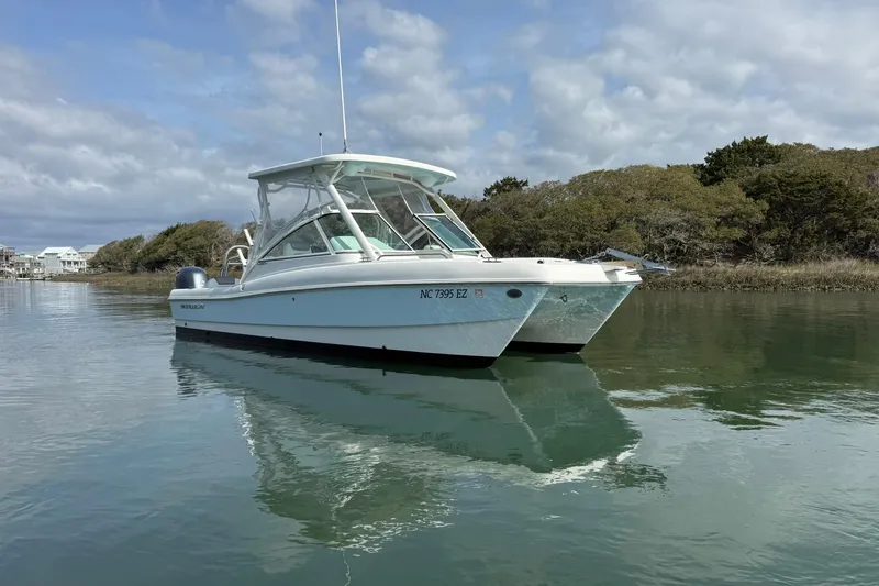 Slide: The Image of 2023 World Cat 230 DC boat on calm water, surrounded by trees and cloudy sky. - 1