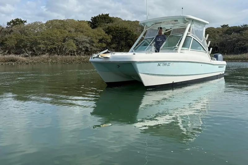 Slide: The Image of 2023 World Cat 230 DC boat on calm water near a wooded shoreline. - 4