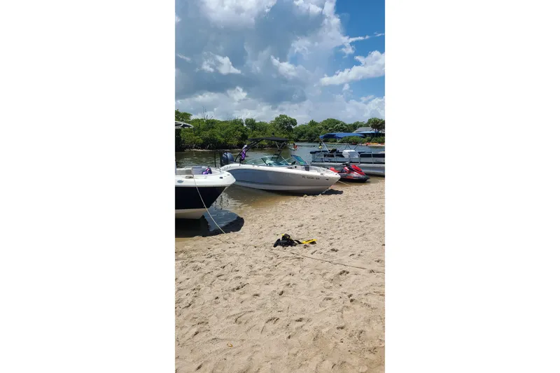 Slide: The Image of Boats and jet skis on a sandy shore under a cloudy sky, featuring a 2020 Chaparral 21 SSi OB. - 7