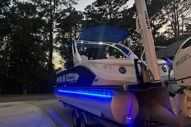 Slide: The Image of 2020 Manitou 25 X-Plode RFW pontoon boat with blue LED lights, parked outdoors. - 6