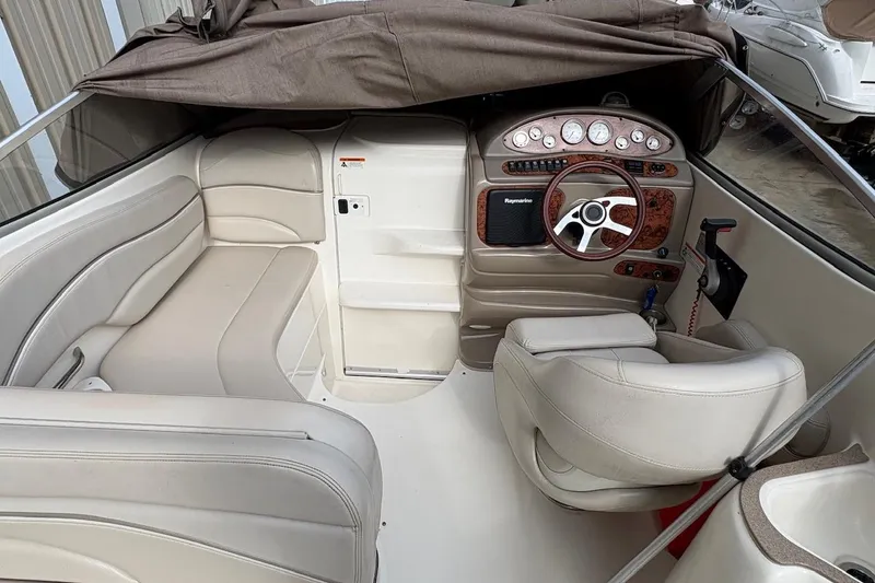 Slide: The Image of 2006 Larson Cabrio 260 boat interior with beige seating and wood-accented dashboard. - 14