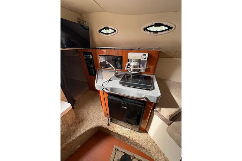 Slide: The Image of 2006 Larson Cabrio 260 cabin interior with kitchenette, featuring stove, coffee maker, and compact fridge. - 4