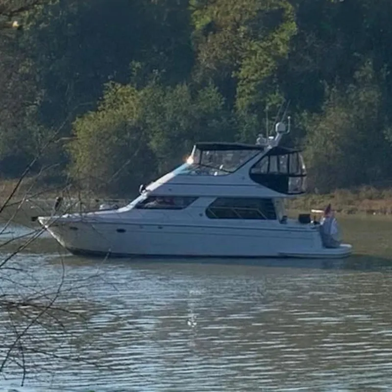 The Image of 1999 Carver 450 Voyager Pilothouse yacht cruising on a serene river with lush greenery. - 0