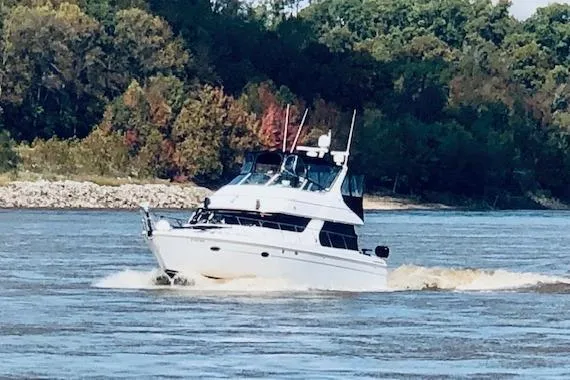 Slide: The Image of 1999 Carver 450 Voyager Pilothouse cruising on a river with lush forest backdrop. - 2