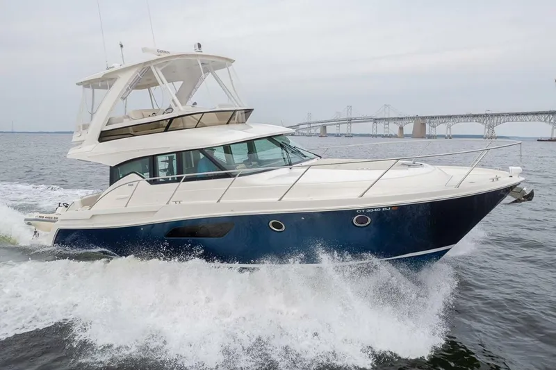 The Image of 2021 Tiara Yachts F44 Flybridge cruising on water near a bridge. - 1