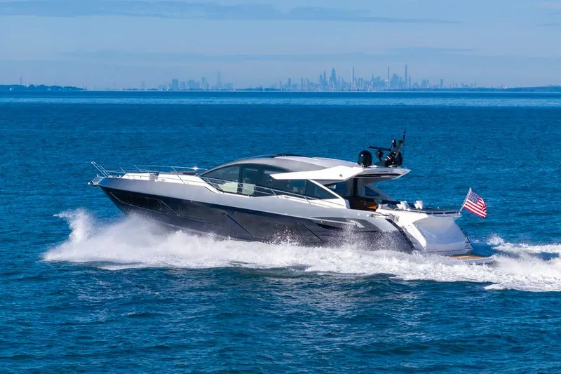 Slide: The Image of 2020 Sunseeker Predator 74 yacht cruising on open water with city skyline in background. - 12