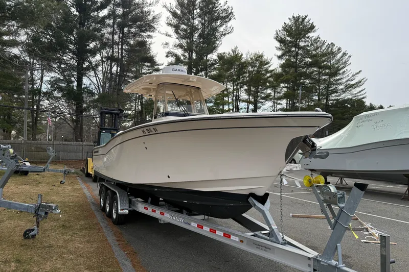 Slide: The Image of 2024 Grady-White Canyon 271 boat on trailer in parking lot, surrounded by trees. - 5
