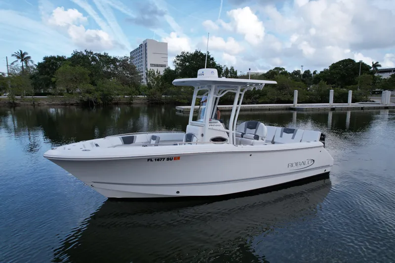 The Image of 2021 Robalo R230 Center Console boat on calm water, surrounded by trees and buildings. - 0