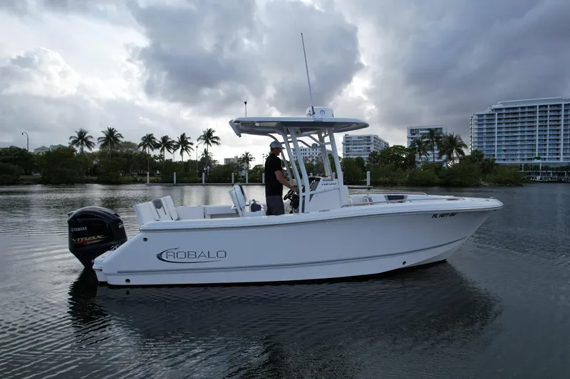 Slide: The Image of 2021 Robalo R230 Center Console boat on calm water, with palm trees and buildings in background. - 3