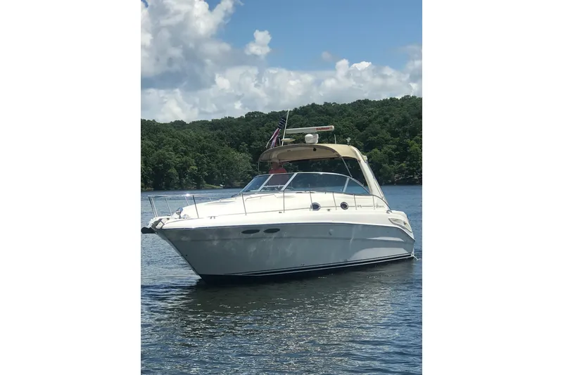 The Image of 2001 Sea Ray 340 Sundancer yacht on a serene lake with lush green backdrop. - 0
