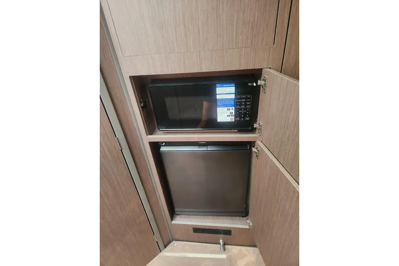 Slide: The Image of 2025 Beneteau Gran Turismo 32 interior with microwave and mini fridge in wooden cabinetry. - 34