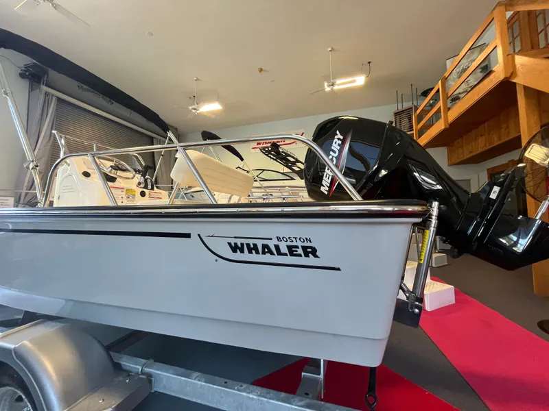 Slide: The Image of A 2026 Boston Whaler 150 Montauk sits on a trailer in a showroom. - 11