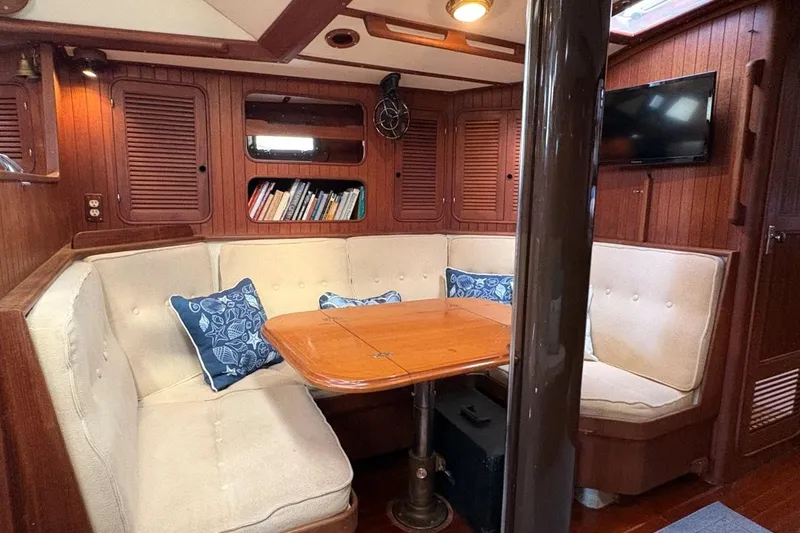 Slide: The Image of Cozy 1981 Norseman 447 yacht interior with cushioned seating, wooden table, and bookshelves. - 26
