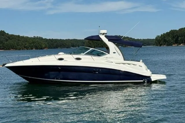 The Image of 2006 Sea Ray Sundancer 320 yacht cruising on a serene lake with lush green shoreline. - 0