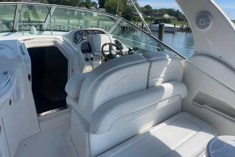 Slide: The Image of 2003 Sea Ray 300 Sundancer cockpit with white seating and steering wheel, docked by the water. - 6
