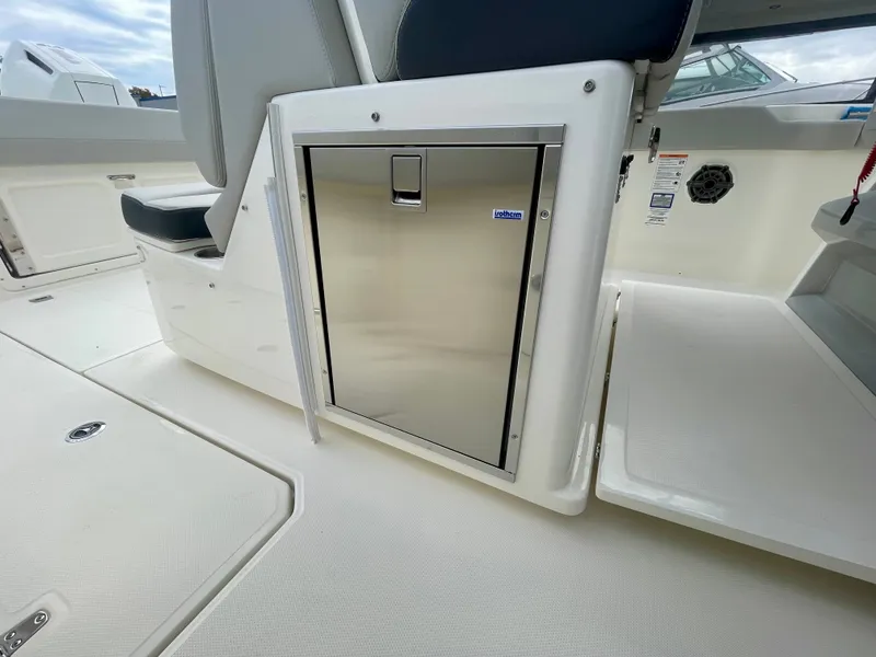 Slide: The Image of The image shows the interior of a 2027 Boston Whaler 330 Outrage with a stainless steel refrigerator. - 14