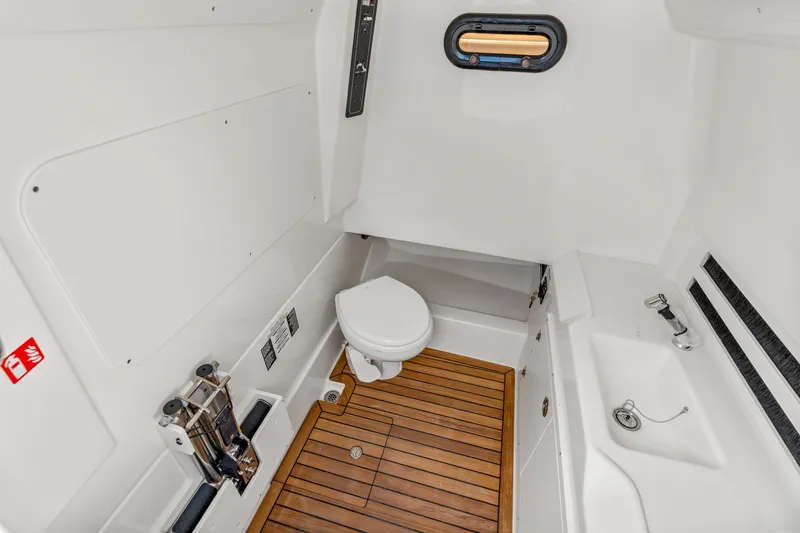 Slide: The Image of The cabin of the 2027 Boston Whaler 330 Outrage features a toilet and sink with wooden flooring. - 19