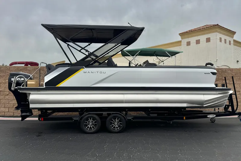 The Image of 2025 Manitou EXPLORE 24 pontoon boat on trailer, featuring sleek design and Suzuki engine. - 0