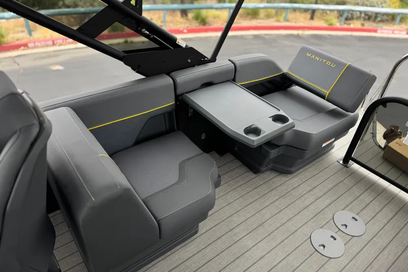 Slide: The Image of 2025 Manitou EXPLORE 24 boat interior with gray seating and table, featuring cup holders. - 17
